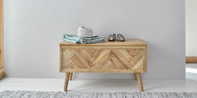 Parquet blanket box in a hallway with a hat, scarf and shoes on top.