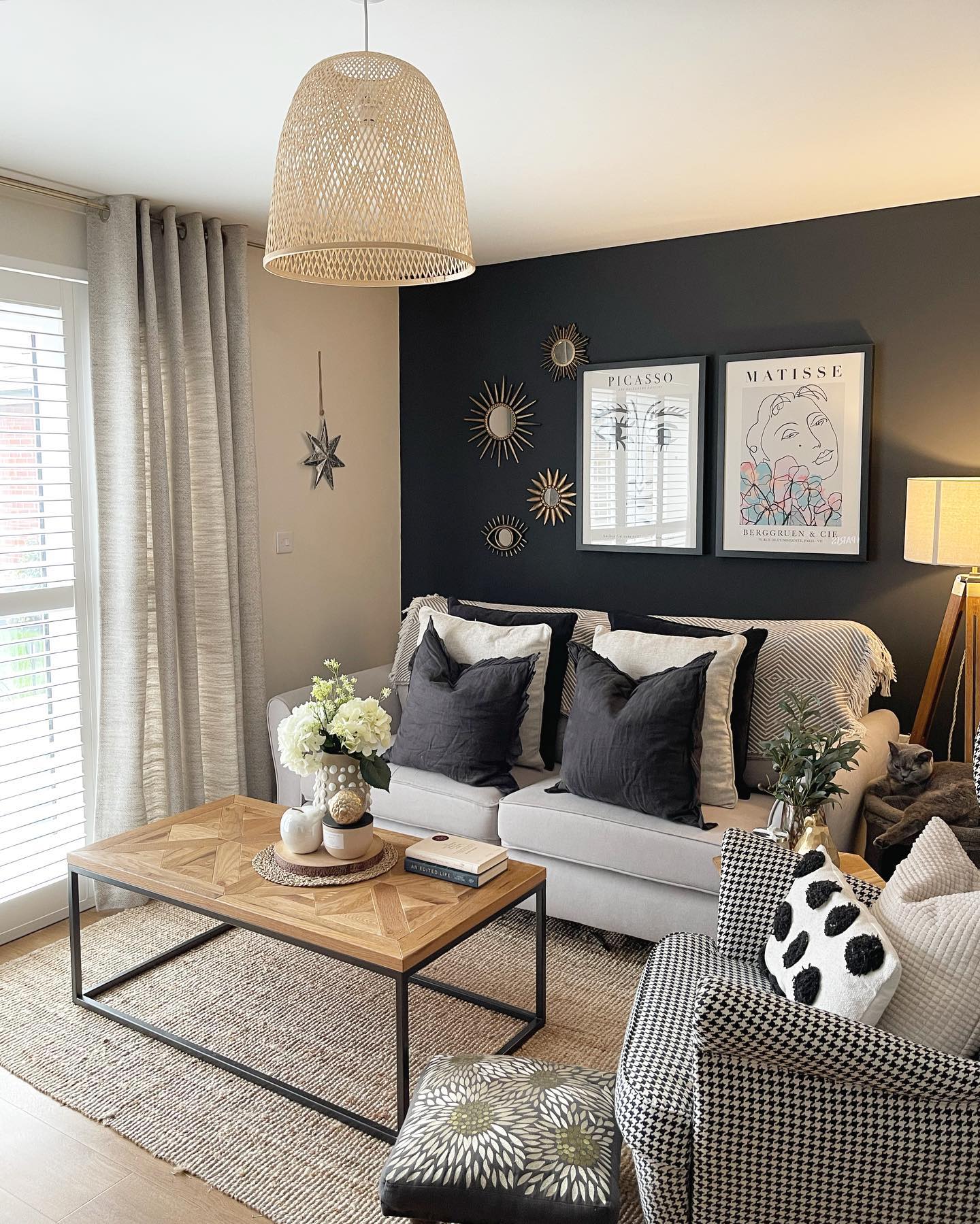 A sofa-living room furniture-beige sofa-houndstooth armchair-charcoal feature wall-monochrome cushions-wood and metal coffee table-wicker lampshade-floor standing lamp-jute rug-neutral linen curtain-wooden flooring-abstract wall art