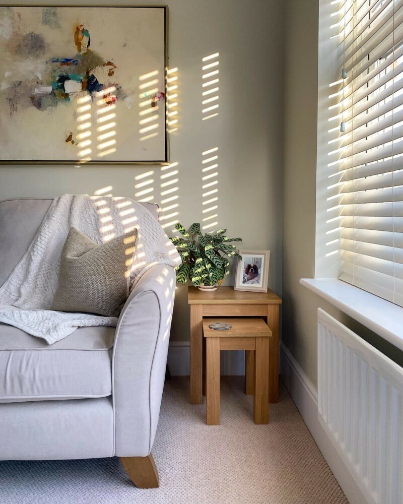 Neutral sofa in sun-dappled living room with a nest of tables, plants and colourful artwork.