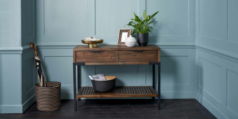 Oak Furnitureland Detroit dark glazed console table against a blue backdrop.