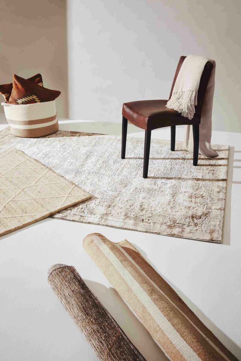 Collection of cream rugs on the floor and two rolled up, with a brown leather chair also in shot.