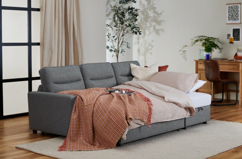 Multipurpose home office space with a desk in the background and an open sofa with bedding ready to welcome guests.