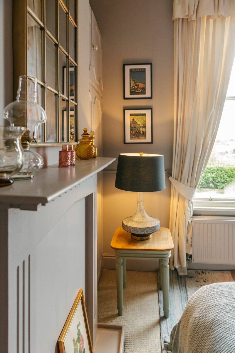 Close up of a period fireplace with a gold mirror hanging above a mantelpiece that’s decorated with delicate vases.