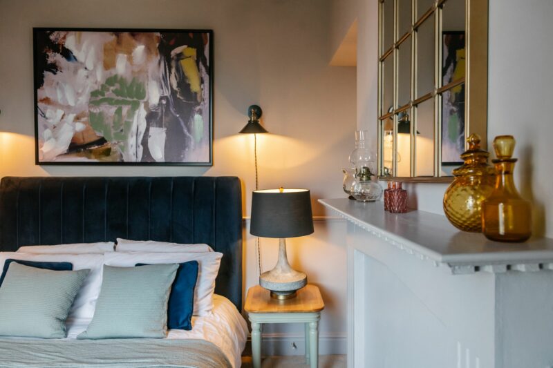Dark blue velvet upholstered bed with colourful artwork hung above in an elegant room in a period home.