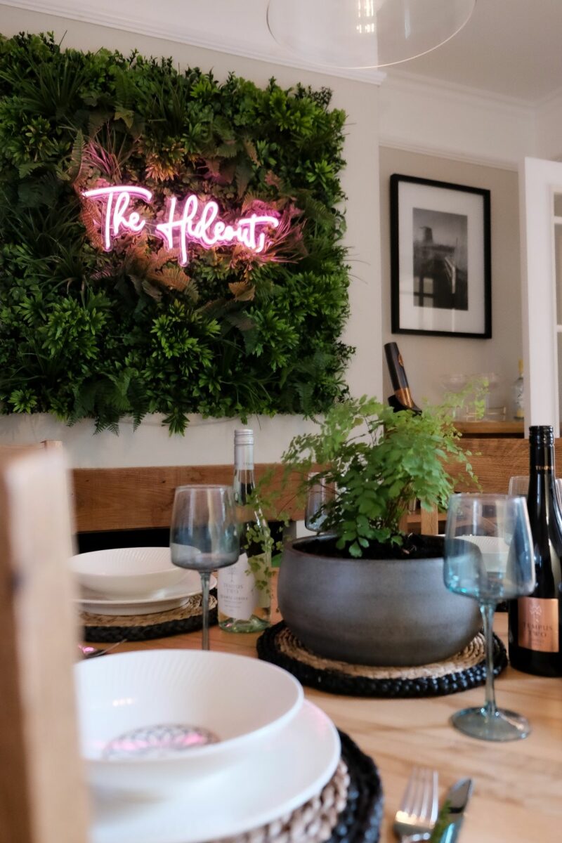Oak Furnitureland Knightsbridge dining table styled with crockery and neon sign in the background.
