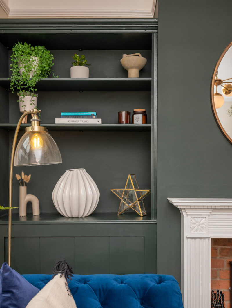 Oak Furnitureland blue Montgomery velvet sofa next to floor lamp and built in shelving filled with decorative accessories.