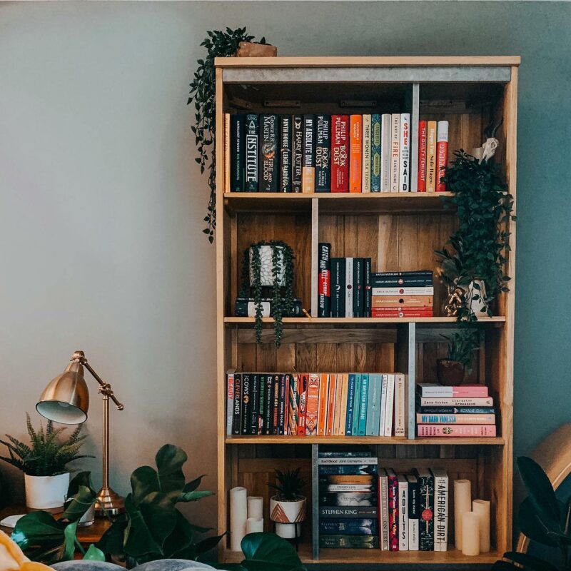 Oak Furnitureland Boston oak and metal bookcase filled with colourful books and styled with plants.