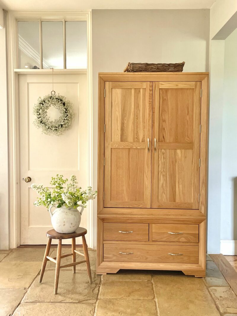 Bevel natural oak freestanding larder in neutral kitchen with flowers and green wreath.