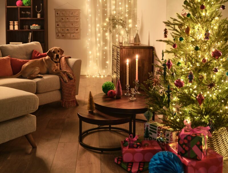 Cream corner sofa with a dog sitting on surround by a Christmas tree, presents and decorations.