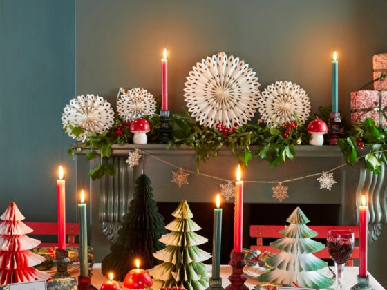 Red, white, and green Christmas tablescape, with a decorated fireplace behind including paper decorations and candles.
