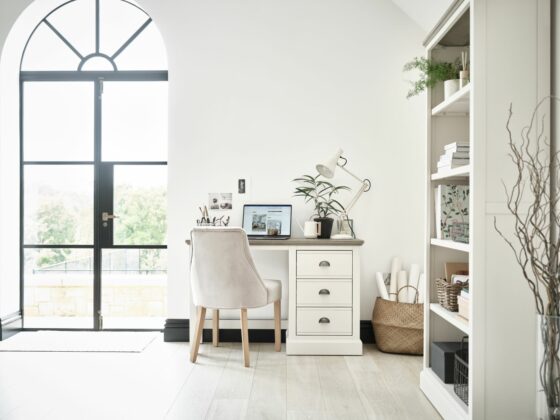 White painted desk paired with a grey velvet chair in a light and airy white home office with a large door out to the garden.