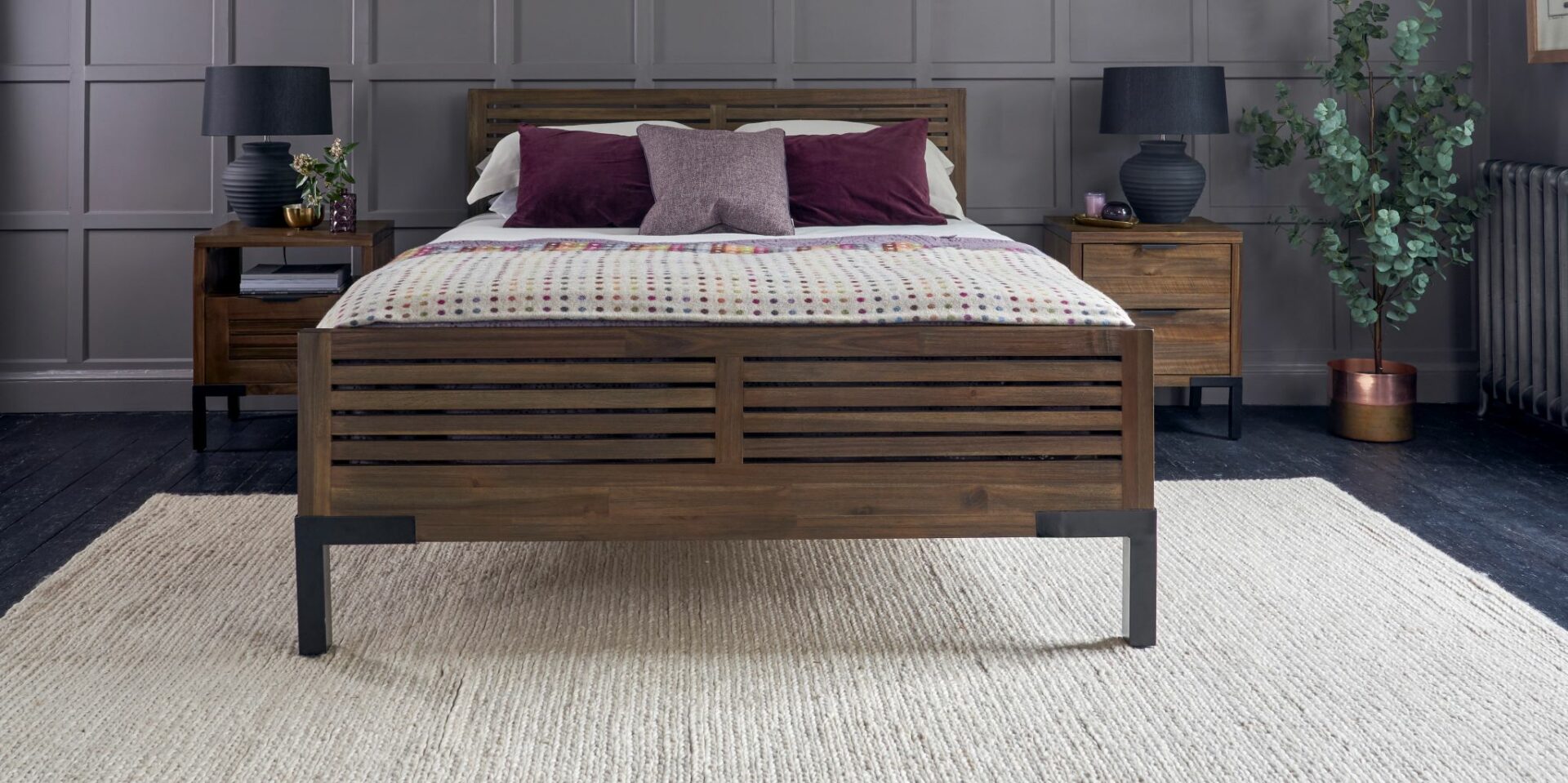 Dark stained oak and metal bed with matching bedside tables with black table lamps.