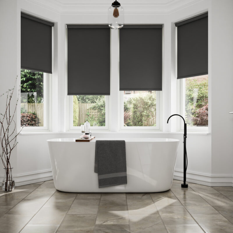 Freestanding bath in bay window with dark grey blinds.