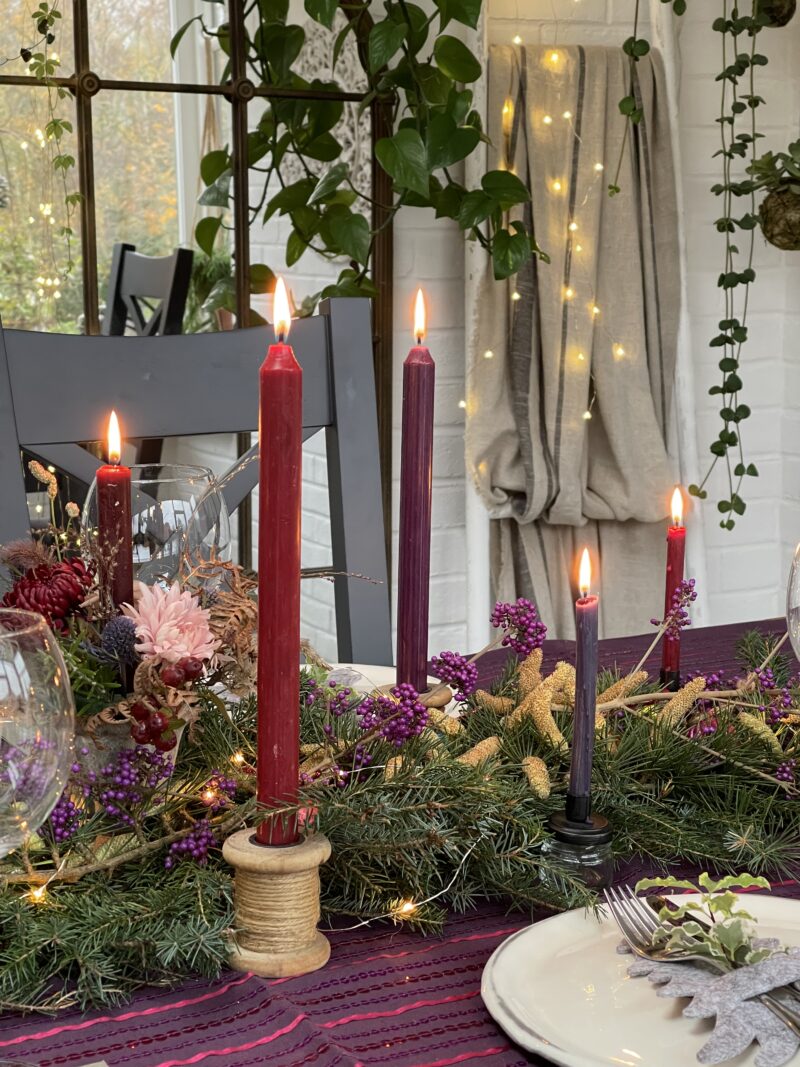 A dining table and wall mirror-dining room furniture-purple tabelcloth-festive centrepiece-tapered candles-black metal mirror-grey dining chair-foliage