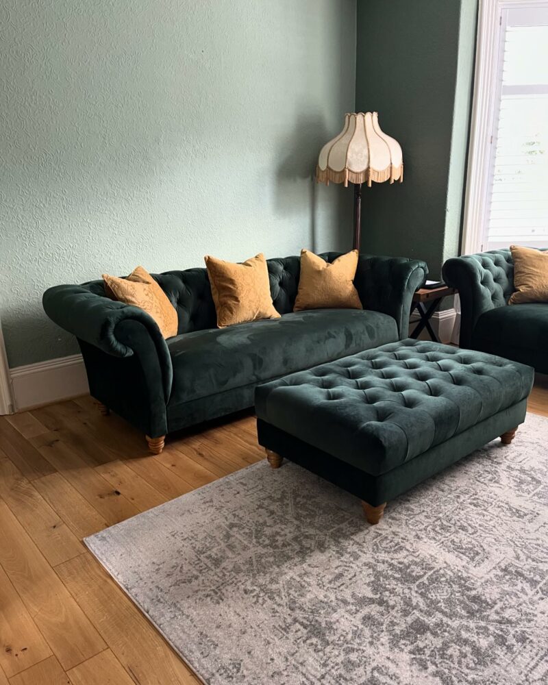 A sofa and footstool-living room furniture-plush velvet green sofa-mustard cushions-patterned rug-soft green walls-antique floor lamp