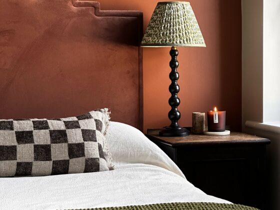 A bed, bedside tables, table lamps-bedroom furniture-terracotta walls-amber glass candle-checkered cushion-bobbin lamps-dark wooden bedside table-rust red velvet headboard- green throw-white bed linen