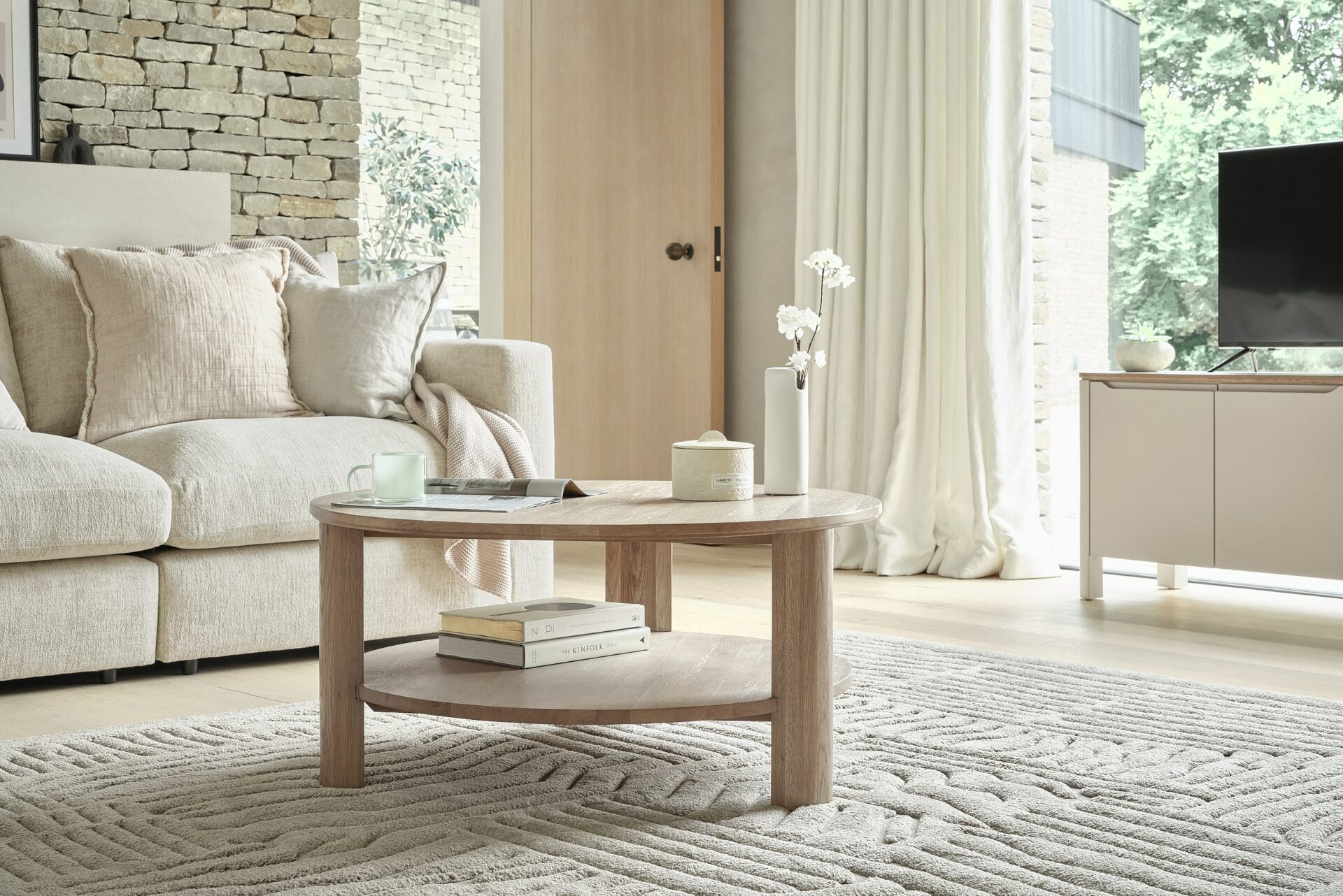 A sofa, coffee table, and TV unit-living room furniture-textured neutral rug-pale oak coffee table-cream sofa-neutral TV unit-clever storage-exposed brick walls-cream draped curtains