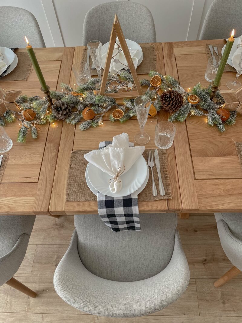 A dining table and chairs-dining room furniture-wooden tabletop-upholstered grey dining chairs-festive centrepiece-check napkins-white crockery-jute placemats-green candles