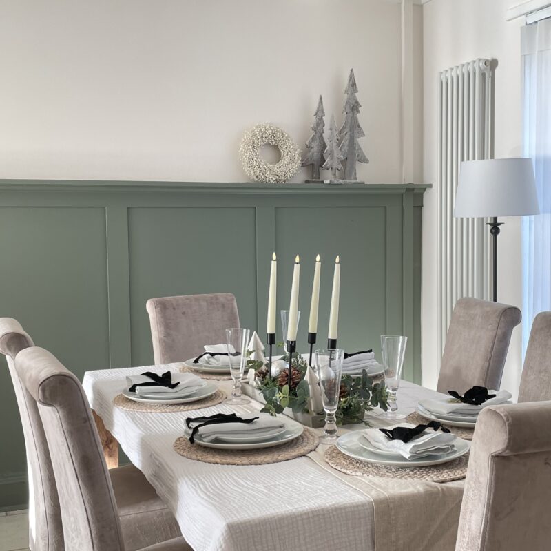 A dining table and chairs-dining room furniture-black candle holders-green panelling-silver Christmas trees-mink scroll back chairs-white crockery-jute placemats