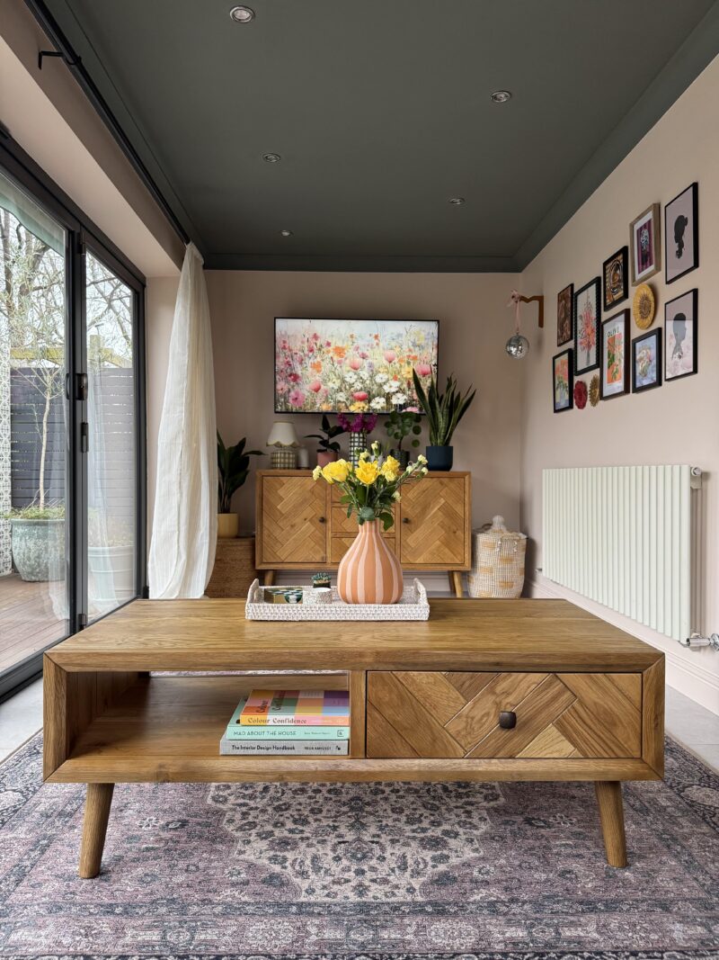 A coffee table and TV unit-stylish living room-wooden coffee table with geometric design-matching wooden TV unit-gallery wall-warm neutral walls-patterned rug-fresh flowers in striped vase-floral image on TV