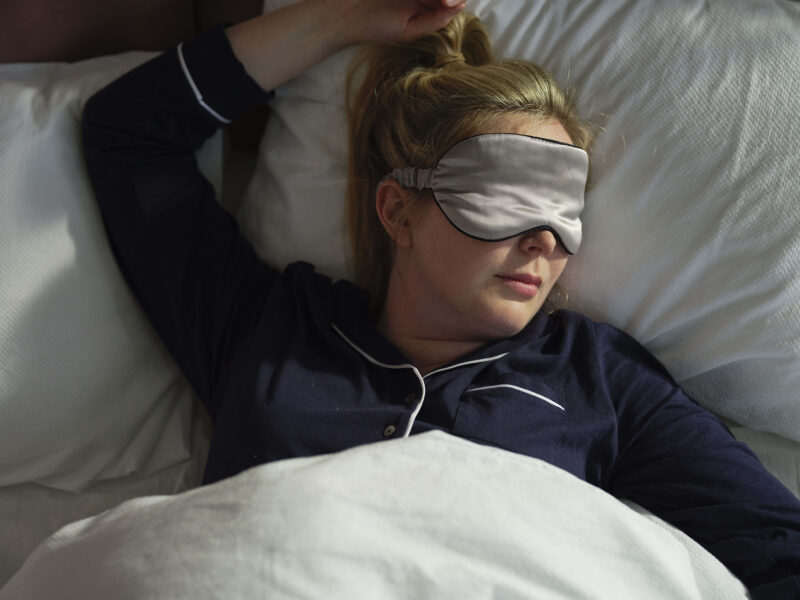 A woman in a bed-bedroom furniture-a woman sleeping in bed-white linen bedding-eye mask-navy blue pjs