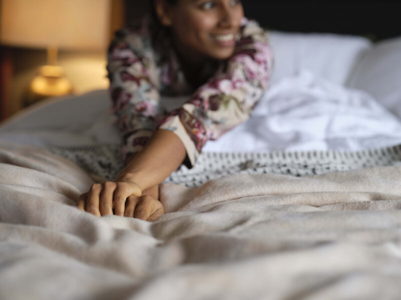A woman in a bed-bedroom furniture-a woman stretching in bed-white linen bedding-cosy neutral throw-floral pjs