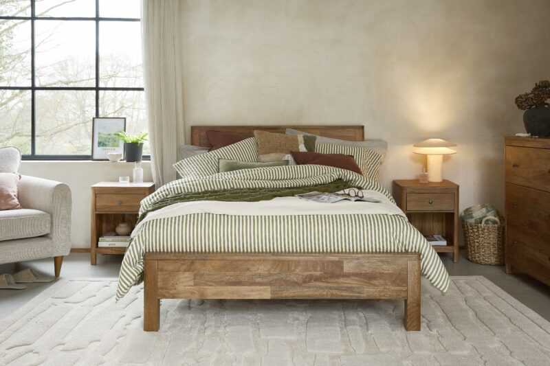 A bed, bedside tables, chest of drawers, and armchair-bedroom furniture-mango wood bed-modern neutral lamp-textured neutral rug-neutral walls-cream armchair-house plants-wall art