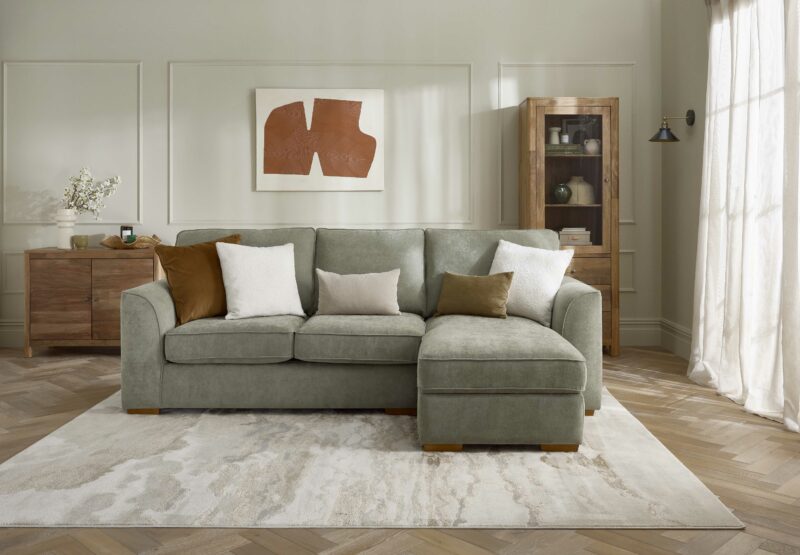 A sofa bed-living room furniture-green corner chaise sofa bed-beaded neutral walls-mango wood sideboard-display cabinet-abstract wall art-neutral rug-parquet floor-sheer curtain-block colour cushions