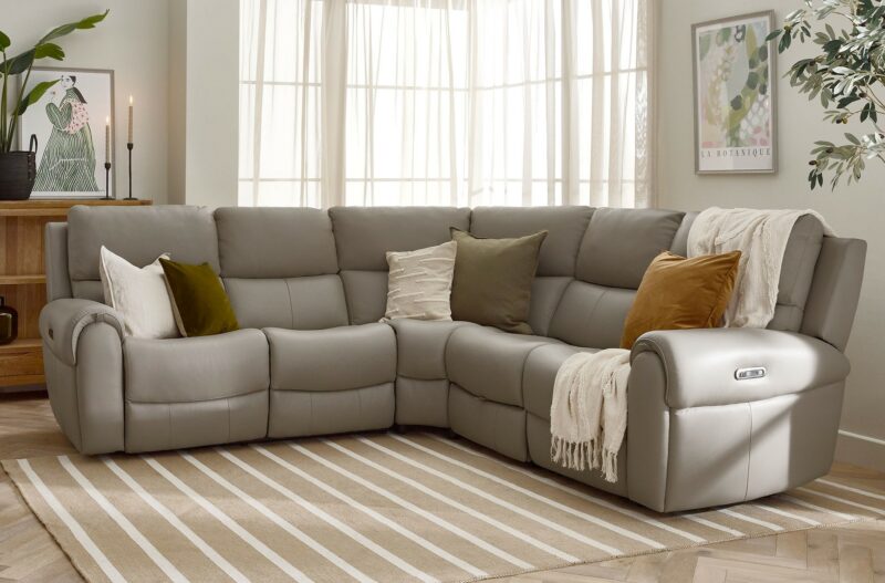 A recliner corner sofa-living room furniture-leather corner sofa-accent cushions-striped rug-parquet floor-wooden bookcase-statement wall art-house plants-cream throw-natural light