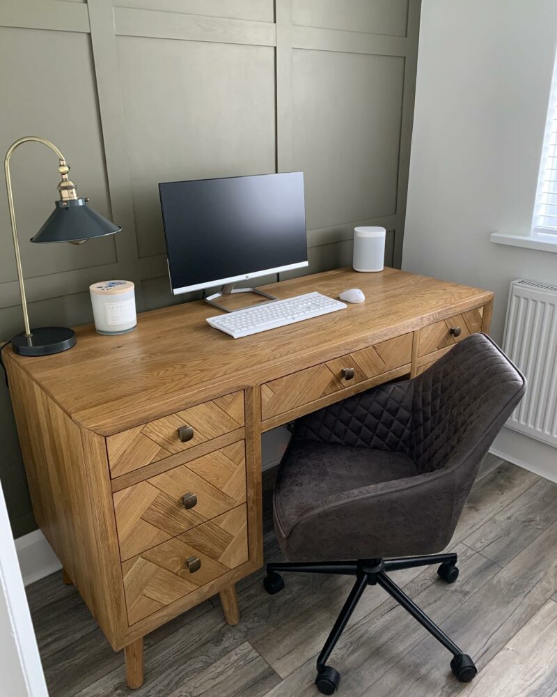 A desk and chair-home office furniture-oak desk with drawers-brown leather office chair-wooden floor-green panelled walls-vintage style desk lamp-desktop computer-scented candle-smart speaker