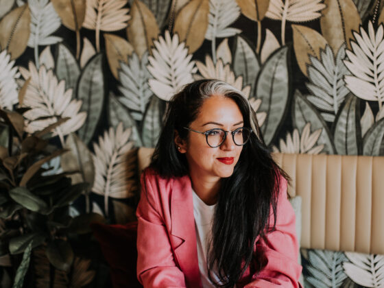 A woman in a restaurant-dining room-feature foliage wallpaper-marble topped table-cream leather banquet seating-pink blazer