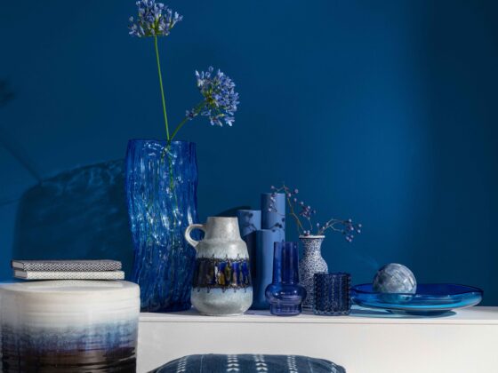 A shelf and vases-living room furniture-dark blue wall-wooden floor-white shelf-blue cushions-various blue vases