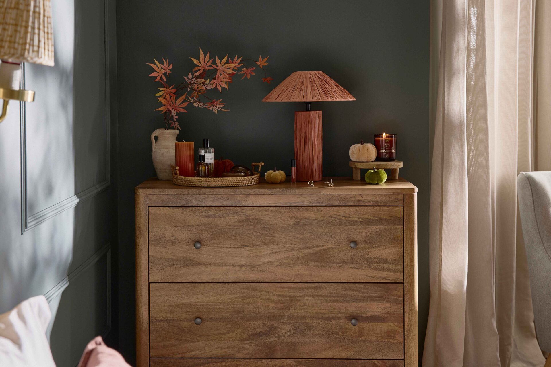A chest of drawers-bedroom furniture-mango wood chest of drawers-rich blue walls-beige draped curtains-rust table lamp-velvet pumpkin decor-woven tray-ceramic pot-amber candle-perfume-wall mounted light-wall beading