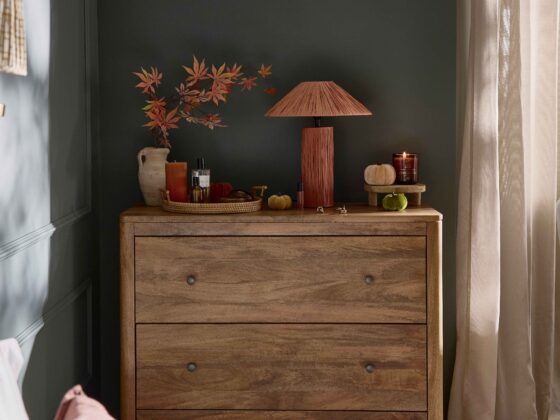 A chest of drawers-bedroom furniture-mango wood chest of drawers-rich blue walls-beige draped curtains-rust table lamp-velvet pumpkin decor-woven tray-ceramic pot-amber candle-perfume-wall mounted light-wall beading