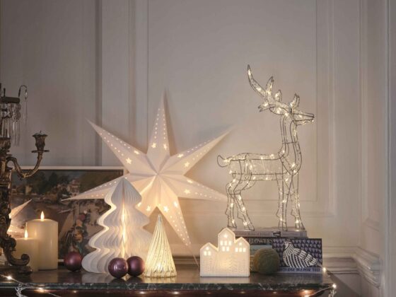 A sideboard-living room furniture-dark wooden sideboard-fairy lights-white star light-wire reindeer light-paper Christmas tree decorations-cream pillar candles-candelabra-painting-purple baubles-white panelled walls