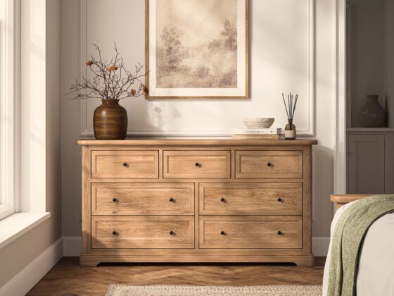A chest of drawers-bedroom furniture-natural oak chest of drawers-parquet flooring-jute rug-brown vase-neutral panelled walls-subtle wall art-green throw-neutral bedding
