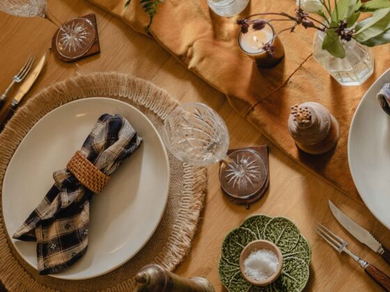 A table-dining room furniture-round wooden dining table-birds eye view-woven natural placemats-off white crockery-fabric table runner-fresh flowers in glass vases-crystal champagne glasses-matches pot-salt bowl-cabbage plate-pepper grinder-candle