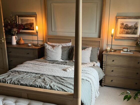A bed and chest of drawers-wooden four poster bed-cushioned bench-neutral bed linen-wooden chest of drawers-wall beading-sage green walls-candle light-framed landscapes-beige carpet