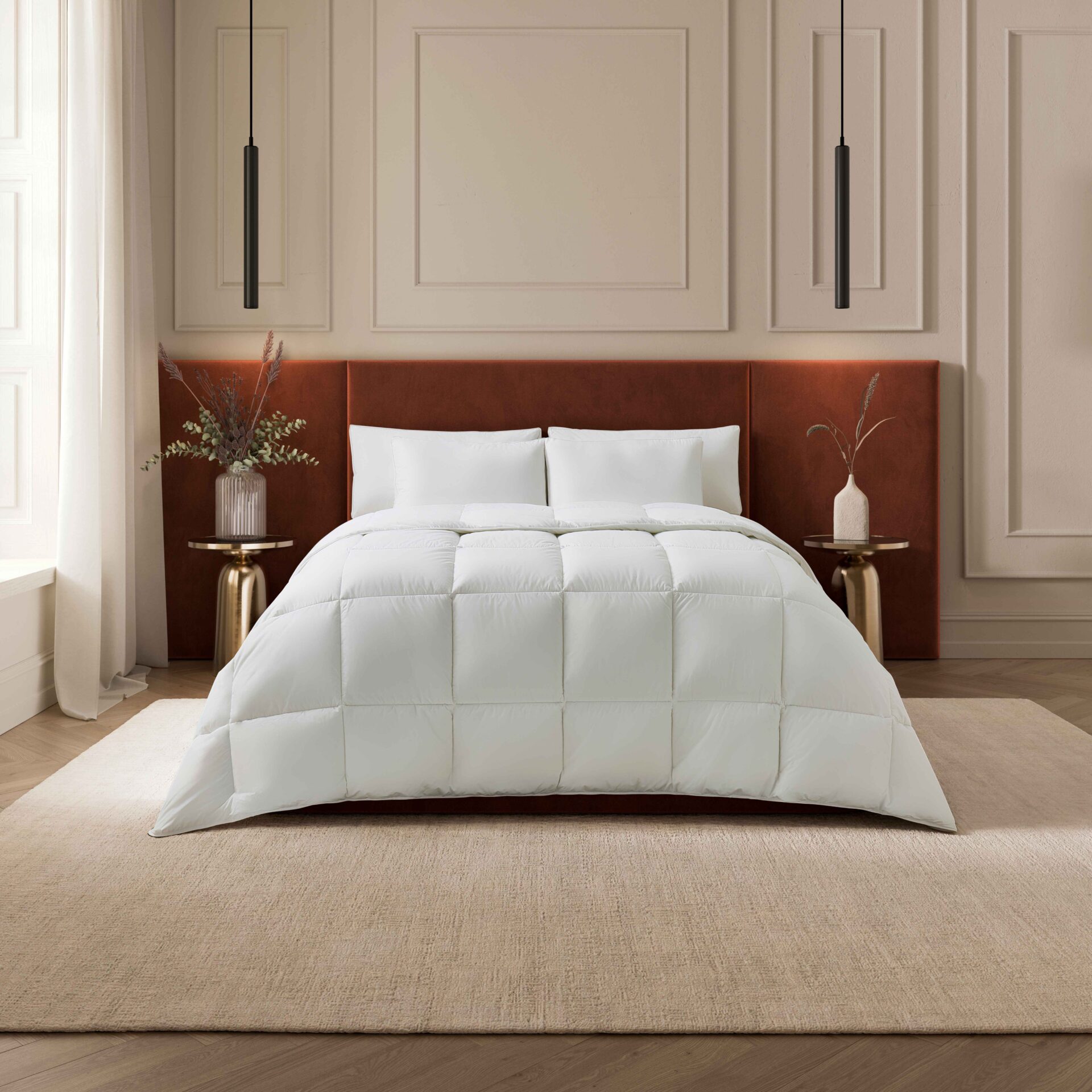 A bed-bedroom furniture-rust coloured velvet headboard-white bed linen-beige walls with beading-brass bedside tables-sheer draped curtains-dried flower vases-beige rug-black pendant lights-parquet wooden floor