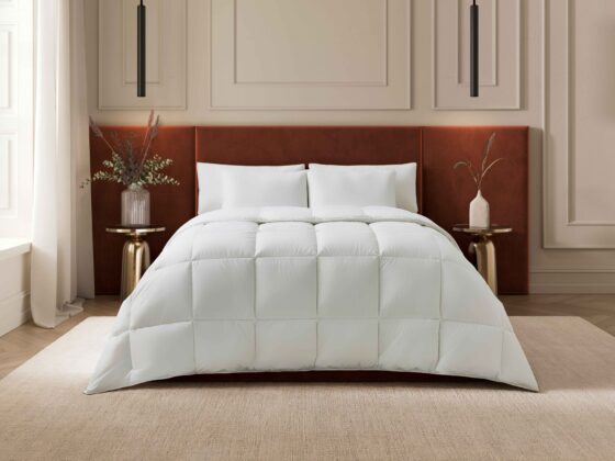 A bed-bedroom furniture-rust coloured velvet headboard-white bed linen-beige walls with beading-brass bedside tables-sheer draped curtains-dried flower vases-beige rug-black pendant lights-parquet wooden floor