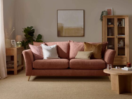 A sofa, coffee table, display cabinet, and console table-living room furniture-terracotta coloured sofa-wooden console table-neutral walls-sisal carpet-cream vase with dried flowers-potted house plant-framed photo-glass lamp-neutral abstract wall art-draped sheer curtain-wooden and glass display cabinet-round wooden coffee table