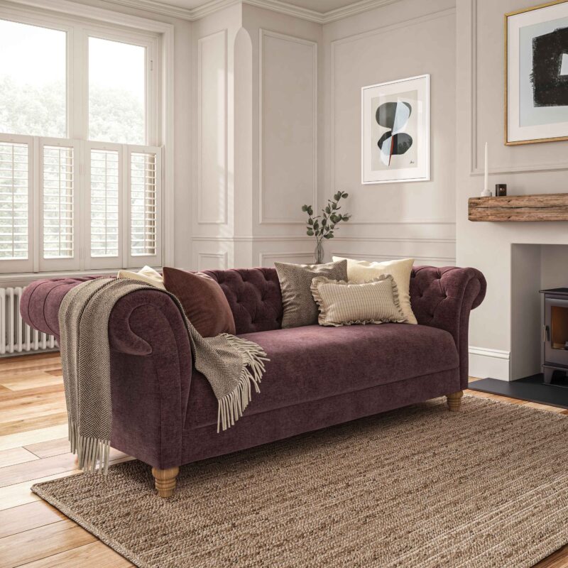 A sofa-living room furniture-mauve coloured chesterfield style sofa-neutral cushions-neutral walls with panelling and beading-abstract artwork-jute rug-fireplace-window shutters-radiator-neutral throw