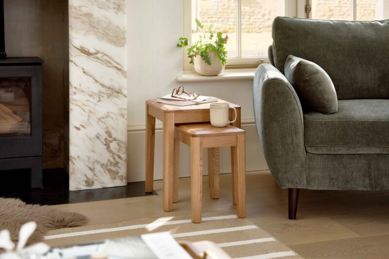 An armchair, side table, and rug-living room furniture-olive green armchair-natural oak nest of tables-cream walls-wooden floor-natural striped jute rug-brown faux sheepskin rug-marble fireplace-ceramic mug-potted plant
