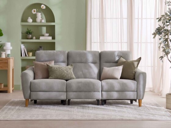 A sofa and console table-living room furniture-grey leather recliner sofa-earthy scatter cushions-vintage style rug-sheer curtains-sage green walls-built in arched shelving-oak console table-potted houseplant-cream vase with white flowers-woven basket-stacked books