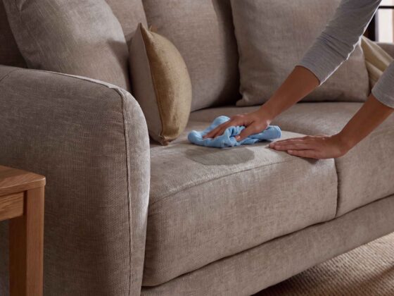 A sofa and side table-living room furniture-beige sofa-scatter cushions-blue cloth-grey top-person cleaning-wooden side table-sisial carpet