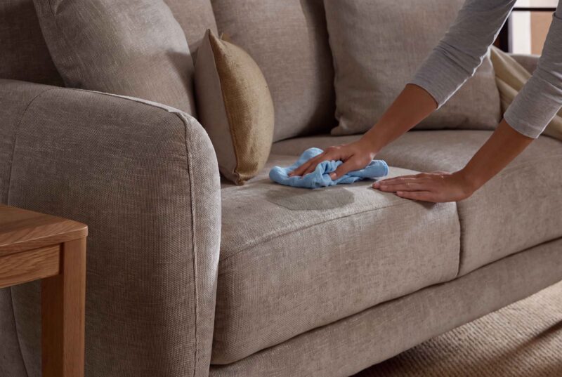 A sofa and side table-living room furniture-beige sofa-scatter cushions-blue cloth-grey top-person cleaning-wooden side table-sisial carpet