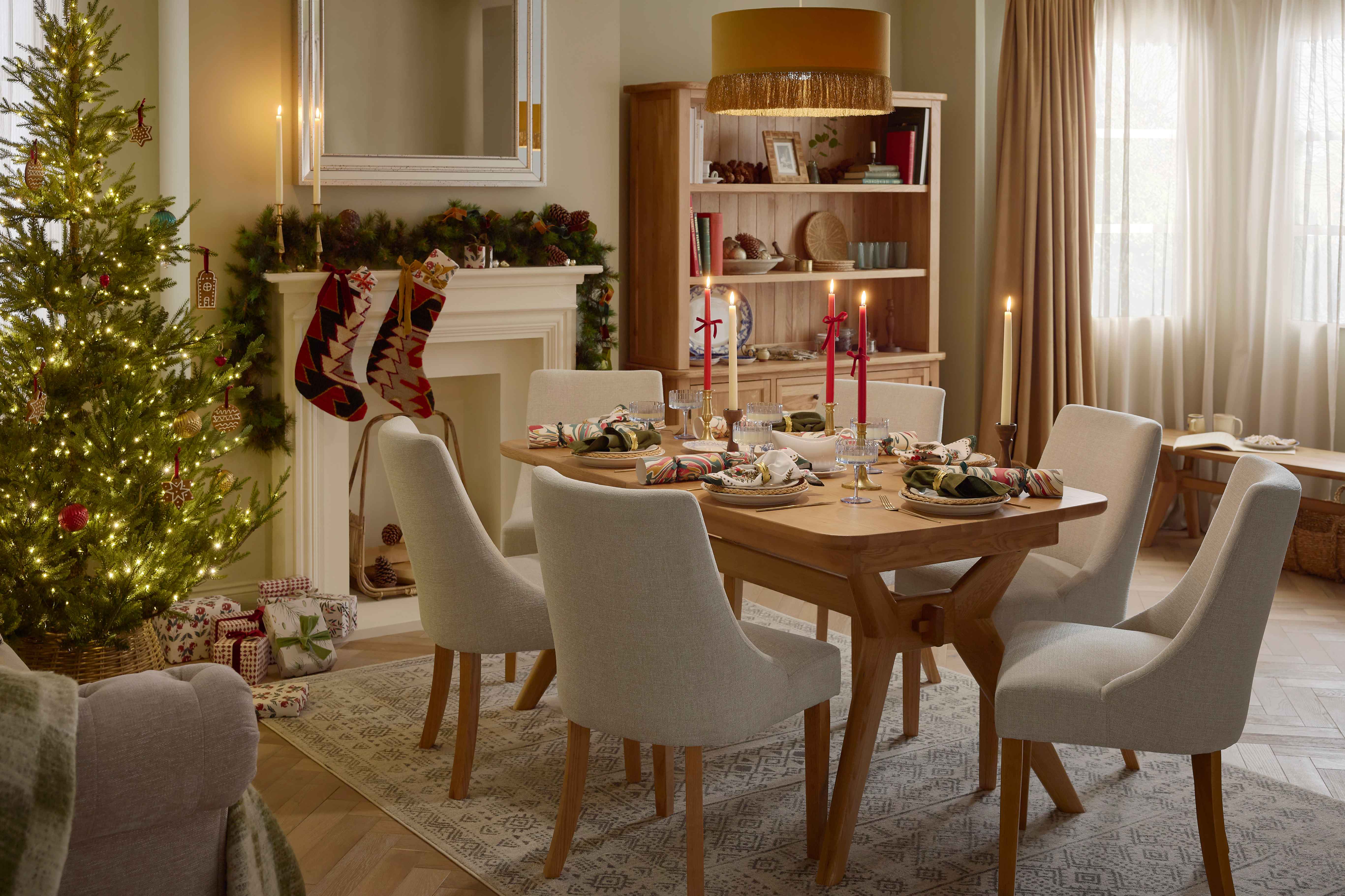 A dining table, chairs, bench, and dresser-dining room furniture-a wooden dining table-beige fabric dining chairs-large wooden dresser-wooden bench-draped curtains-marble patterned crackers-gold cutlery-christmas styling-white gravy boat-tapered candles in red and cream-delicate blue scalloped glassware-white crockery-off white fireplace-festive garland-christmas tree-handmade stockings-mustard tassel ceiling lampshade-wooden bench-vintage style rug-wooden parquet flooring